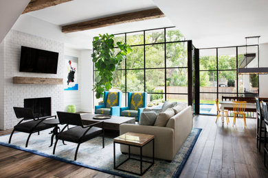 Foto de salón abierto moderno grande con paredes blancas, suelo de madera en tonos medios, marco de chimenea de ladrillo y televisor colgado en la pared