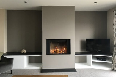 Imagen de salón contemporáneo grande con paredes marrones, moqueta, estufa de leña, marco de chimenea de yeso, televisor independiente y suelo gris