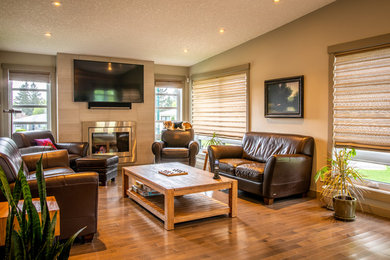 Mittelgroßes, Repräsentatives, Offenes Modernes Wohnzimmer mit beiger Wandfarbe, braunem Holzboden, Kamin, gefliester Kaminumrandung, TV-Wand und braunem Boden in Calgary