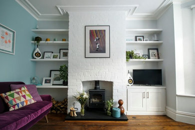 Immagine di un soggiorno moderno di medie dimensioni e chiuso con pareti blu, pavimento in legno massello medio, stufa a legna e cornice del camino in mattoni