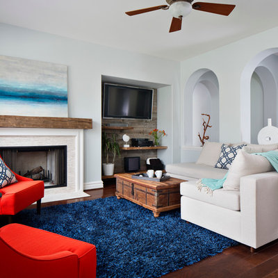Example of a mid-sized beach style open concept medium tone wood floor living room library design in San Francisco with blue walls, a standard fireplace, a wall-mounted tv and a stone fireplace
