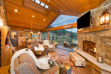 Example of a large mountain style open concept medium tone wood floor and brown floor living room design in Denver with a corner fireplace, a stone fireplace and a wall-mounted tv