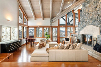 Huge trendy open concept light wood floor, brown floor and exposed beam living room photo in Other with a two-sided fireplace, a stone fireplace, white walls and no tv