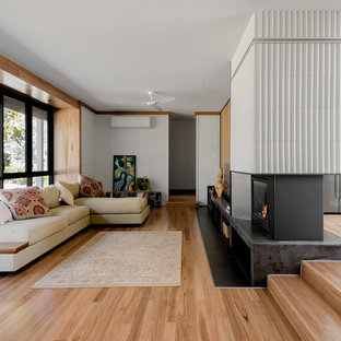 Inspiration for a large midcentury open concept living room in Other with white walls, medium hardwood floors, a two-sided fireplace, a tile fireplace surround, a freestanding tv and brown floor.