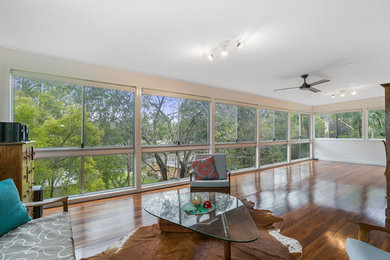 Mittelgroßes Wohnzimmer mit weißer Wandfarbe und braunem Holzboden in Brisbane