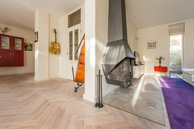 Imagen de salón con rincón musical abierto tradicional renovado de tamaño medio con paredes blancas, suelo de madera clara, estufa de leña, marco de chimenea de metal y televisor colgado en la pared