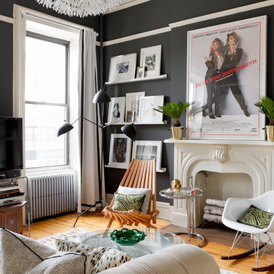 Example of an eclectic medium tone wood floor living room design in New York with black walls, a standard fireplace and a tv stand