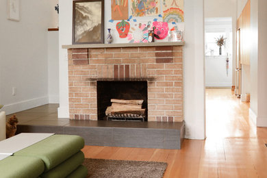 バンクーバーにあるエクレクティックスタイルのおしゃれなリビング (白い壁、淡色無垢フローリング、標準型暖炉、レンガの暖炉まわり) の写真