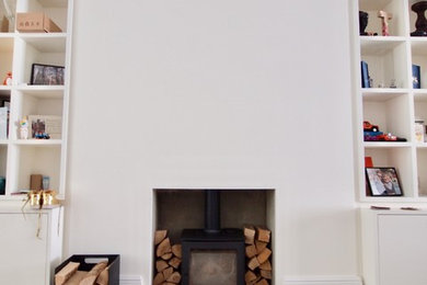 ロンドンにある高級な広いトラディショナルスタイルのおしゃれな独立型リビング (白い壁、無垢フローリング、薪ストーブ、漆喰の暖炉まわり、壁掛け型テレビ、茶色い床) の写真
