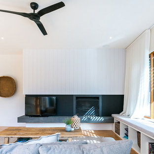 This is an example of a beach style living room in Melbourne with white walls, medium hardwood floors, a standard fireplace, a freestanding tv and brown floor.