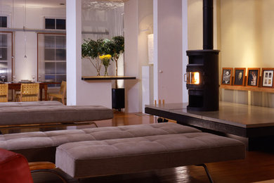 Ejemplo de salón para visitas tipo loft moderno de tamaño medio con paredes multicolor, suelo de madera en tonos medios, estufa de leña, marco de chimenea de hormigón y televisor retractable