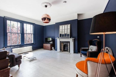 Classic living room in London with blue walls, light hardwood flooring, a standard fireplace and a wooden fireplace surround.