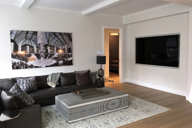 Foto de salón cerrado actual de tamaño medio sin chimenea con paredes beige, suelo de madera clara y televisor colgado en la pared