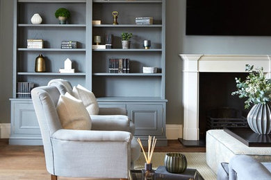 Inspiration for a traditional living room in London with a reading nook, grey walls, medium hardwood flooring, a standard fireplace, a wall mounted tv and brown floors.