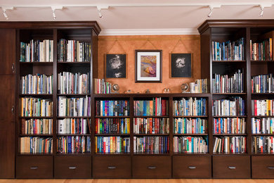 Ejemplo de biblioteca en casa cerrada grande sin chimenea y televisor con parades naranjas y suelo de madera clara