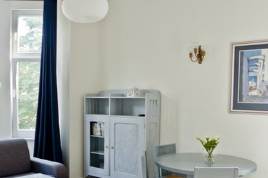 Foto de salón para visitas abierto ecléctico de tamaño medio con paredes beige, suelo de madera clara y televisor retractable