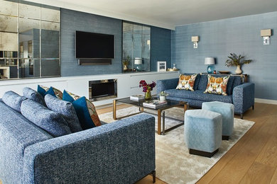 Imagen de salón actual con paredes azules, suelo de madera en tonos medios, todas las chimeneas, televisor colgado en la pared y suelo marrón