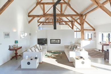 Large contemporary open plan living room in Wiltshire with white walls, concrete flooring, a two-sided fireplace and a freestanding tv.
