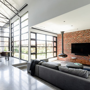 Offenes Industrial Wohnzimmer mit weißer Wandfarbe, Betonboden, Hängekamin, Wand-TV, grauem Boden und Ziegelwänden in Melbourne