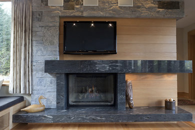 バンクーバーにある中くらいなコンテンポラリースタイルのおしゃれなリビング (ベージュの壁、淡色無垢フローリング、標準型暖炉、石材の暖炉まわり、壁掛け型テレビ) の写真