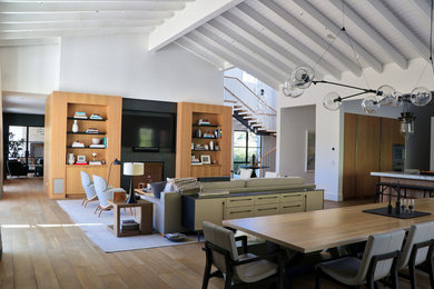 Imagen de salón abierto moderno grande con paredes blancas, suelo de madera clara y televisor colgado en la pared