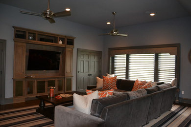 Diseño de salón abierto contemporáneo de tamaño medio sin chimenea con paredes grises, suelo de madera en tonos medios, televisor colgado en la pared y suelo marrón