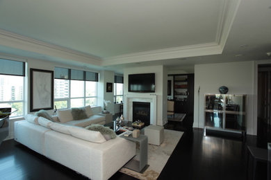 На фото: большая открытая гостиная комната в стиле неоклассика (современная классика) с белыми стенами, темным паркетным полом, стандартным камином и телевизором на стене с