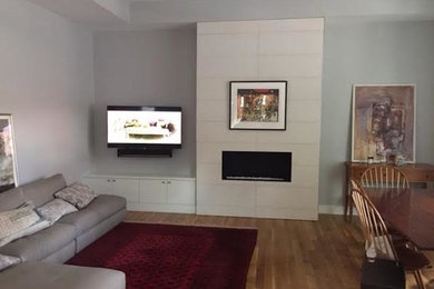 Mittelgroßes, Repräsentatives, Offenes Klassisches Wohnzimmer mit weißer Wandfarbe, braunem Holzboden, Gaskamin, gefliester Kaminumrandung, TV-Wand und braunem Boden in Boston