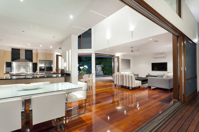 Modelo de salón abierto contemporáneo grande con paredes blancas, suelo de madera oscura y televisor colgado en la pared