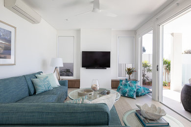 Imagen de salón costero de tamaño medio con paredes blancas, televisor colgado en la pared y suelo beige