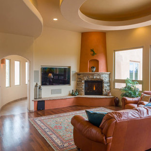 Mid-sized southwest open concept dark wood floor living room photo in Albuquerque with beige walls, a standard fireplace, a stone fireplace and a wall-mounted tv