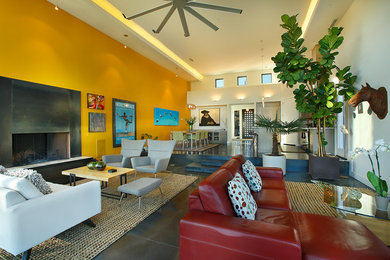 На фото: открытая гостиная комната среднего размера в современном стиле с желтыми стенами, бетонным полом, стандартным камином, фасадом камина из металла, телевизором на стене и коричневым полом