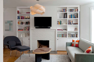 Design ideas for a medium sized scandinavian living room in New York with a brick fireplace surround, a built-in media unit, white walls, medium hardwood flooring and a standard fireplace.