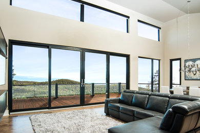Modelo de salón para visitas abierto actual de tamaño medio con paredes blancas, suelo de madera oscura, televisor colgado en la pared y suelo marrón