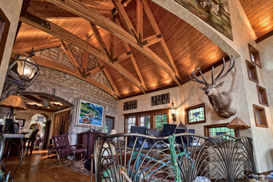 Foto de salón para visitas abierto rural grande con paredes beige, suelo de madera clara, suelo marrón, chimeneas suspendidas y marco de chimenea de piedra