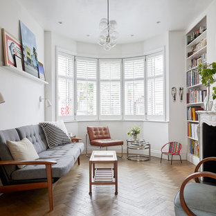 Eclectic enclosed living room in London with white walls, medium hardwood flooring, a standard fireplace, no tv and brown floors.