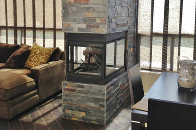 フェニックスにあるコンテンポラリースタイルのおしゃれなリビング (ベージュの壁、ラミネートの床、両方向型暖炉、石材の暖炉まわり、茶色い床) の写真