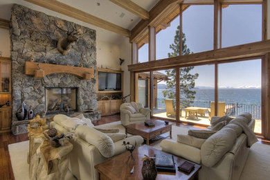 Example of a large mountain style enclosed light wood floor living room design in Sacramento with beige walls, a standard fireplace, a stone fireplace and a media wall