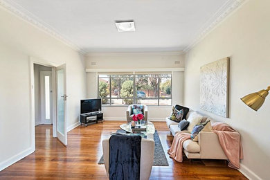 Offenes Wohnzimmer ohne Kamin mit Hausbar, weißer Wandfarbe, braunem Holzboden, freistehendem TV und braunem Boden in Melbourne