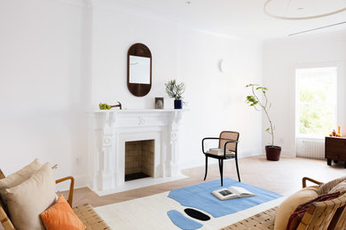 Contemporary formal living room in New York with white walls, light hardwood flooring, a standard fireplace and beige floors.