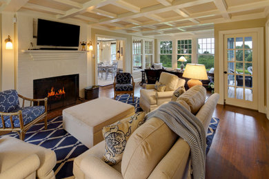 Example of a large beach style formal and open concept medium tone wood floor living room design with beige walls, a standard fireplace, a brick fireplace and a wall-mounted tv