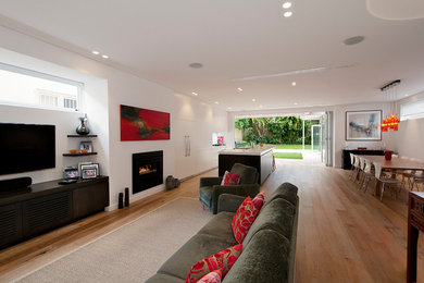 Ejemplo de salón abierto actual de tamaño medio con paredes blancas, suelo de madera clara, estufa de leña, marco de chimenea de metal y televisor colgado en la pared