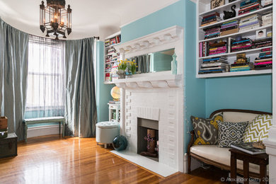 Imagen de biblioteca en casa ecléctica pequeña sin televisor con paredes azules, suelo de madera clara, todas las chimeneas y marco de chimenea de ladrillo