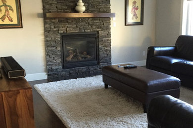 Example of a mid-sized trendy enclosed dark wood floor and brown floor living room design in Edmonton with gray walls, a standard fireplace and a stone fireplace