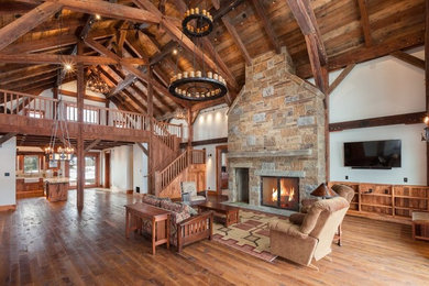 Large mountain style enclosed medium tone wood floor and brown floor living room photo in Other with white walls, a standard fireplace, a stone fireplace and a wall-mounted tv