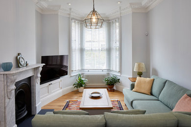 Modelo de salón cerrado actual de tamaño medio con paredes grises, suelo de madera clara, televisor colgado en la pared y suelo beige