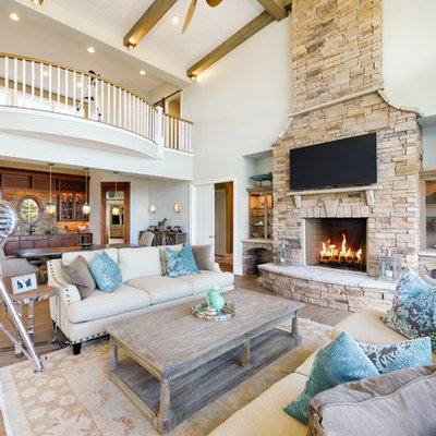 Example of a beach style open concept medium tone wood floor living room design in Other with a stone fireplace, a wall-mounted tv, a standard fireplace and white walls
