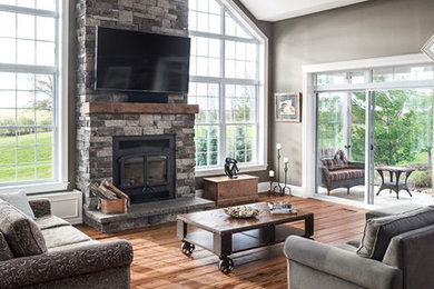 Example of a farmhouse open concept medium tone wood floor and brown floor living room design in Toronto with green walls, a standard fireplace, a brick fireplace and a wall-mounted tv