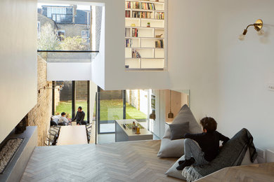 Imagen de biblioteca en casa abierta actual grande con paredes blancas, suelo de madera en tonos medios, chimenea lineal, marco de chimenea de hormigón y televisor colgado en la pared
