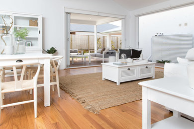Modelo de salón abierto costero de tamaño medio con paredes blancas y suelo de madera en tonos medios